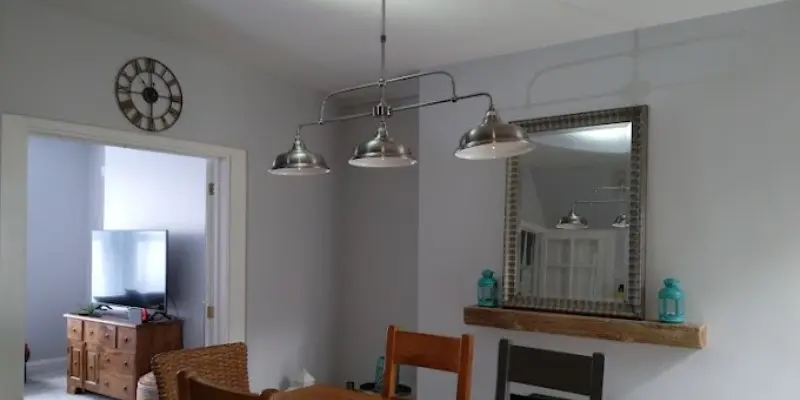A newly installed modern three-bulb chrome pendant light fixture hanging above a dining room table in a Plymouth home.