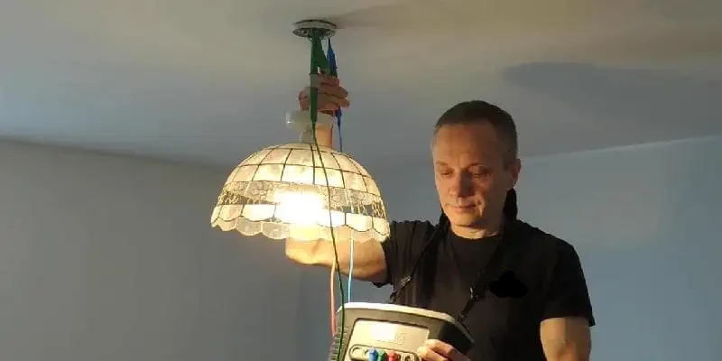 A professional electrician in Plymouth performs an electrical safety and compliance test on a home's ceiling pendant lighting fixture.