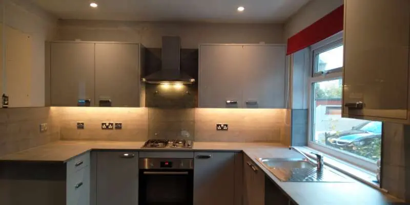Warm under-cabinet LED strip lighting and modern chrome plug sockets installed in a newly renovated grey gloss kitchen by a local Plymouth electrician.